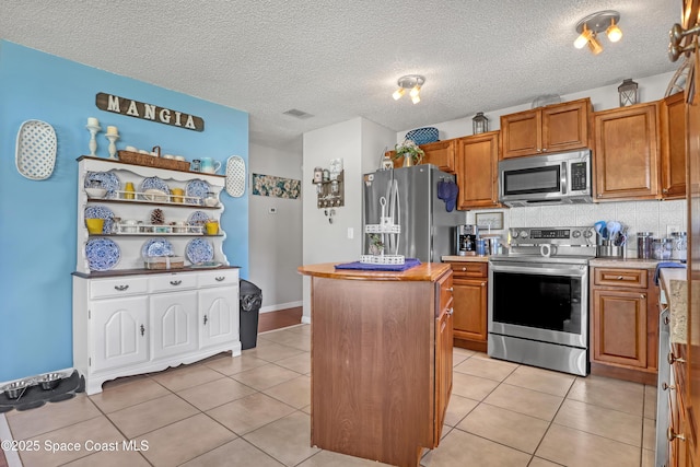 kitchen featuring a textured ceiling, appliances with stainless steel finishes, a kitchen island, tasteful backsplash, and light tile patterned floors