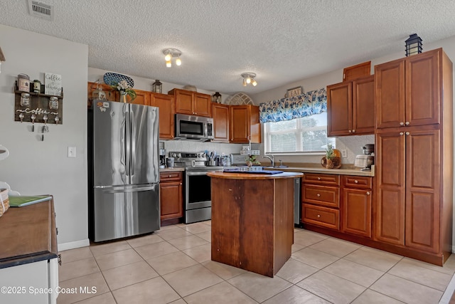 kitchen with light tile patterned floors, appliances with stainless steel finishes, a textured ceiling, and a center island