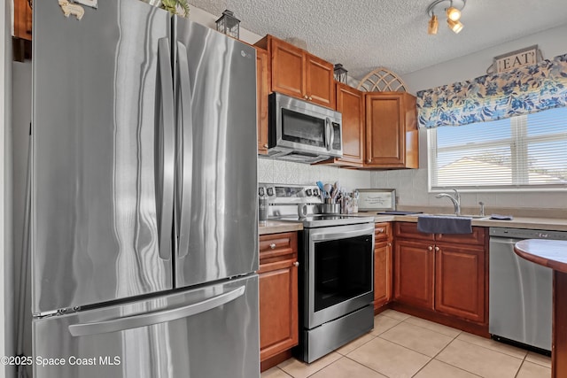 kitchen with sink, a textured ceiling, appliances with stainless steel finishes, and light tile patterned flooring