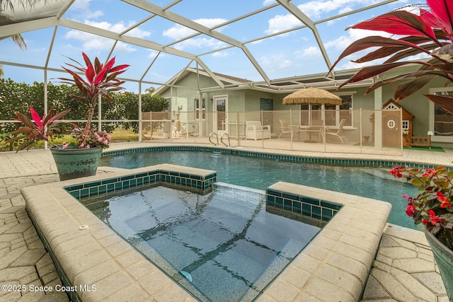 view of pool with a patio, glass enclosure, and an in ground hot tub