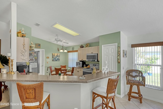 kitchen with kitchen peninsula, appliances with stainless steel finishes, a kitchen breakfast bar, ceiling fan, and light tile patterned floors