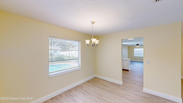 spare room with ceiling fan with notable chandelier, a textured ceiling, light hardwood / wood-style floors, and plenty of natural light