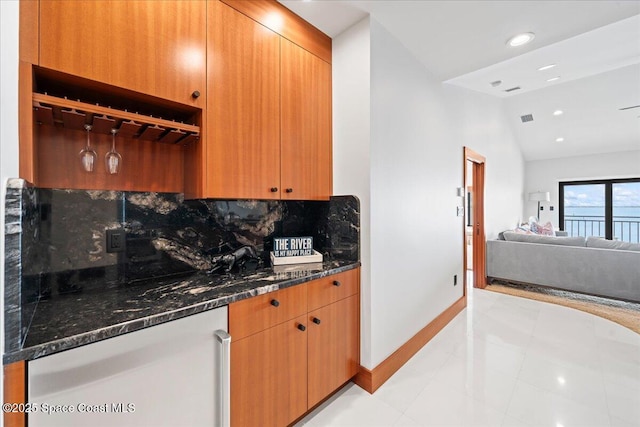 kitchen featuring dark stone counters, light tile patterned floors, decorative backsplash, and lofted ceiling