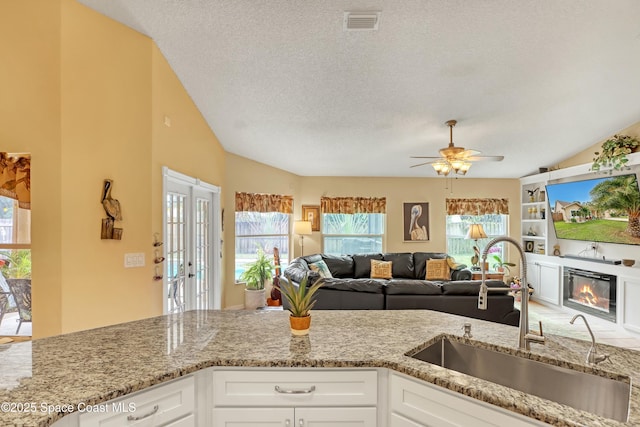 kitchen with light stone counters, a textured ceiling, lofted ceiling, white cabinetry, and sink