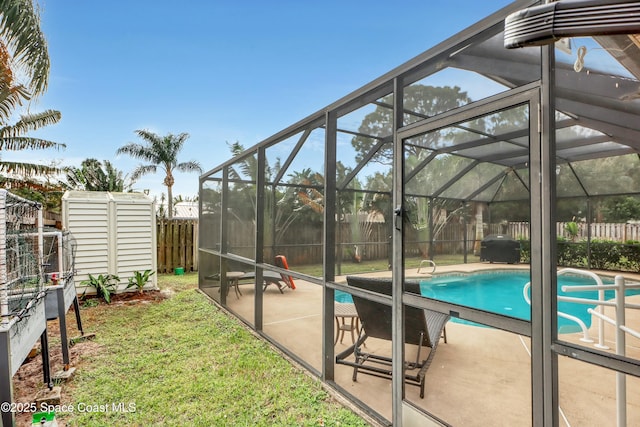 view of pool featuring a lawn, glass enclosure, a storage shed, and a patio area