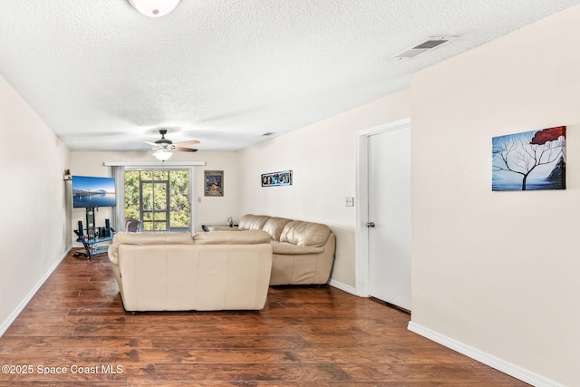 living room with a textured ceiling, ceiling fan, and dark wood-type flooring