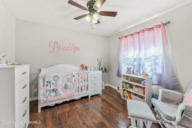 bedroom featuring a crib, a textured ceiling, ceiling fan, and dark wood-type flooring