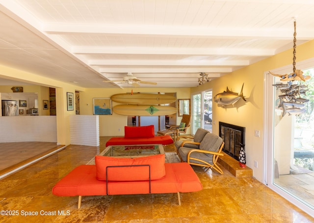 living room with ceiling fan, a glass covered fireplace, and beam ceiling