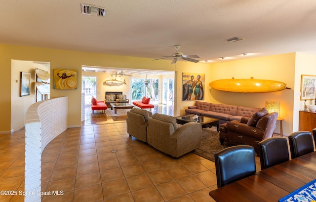 tiled living room featuring a ceiling fan, a glass covered fireplace, visible vents, and a textured ceiling