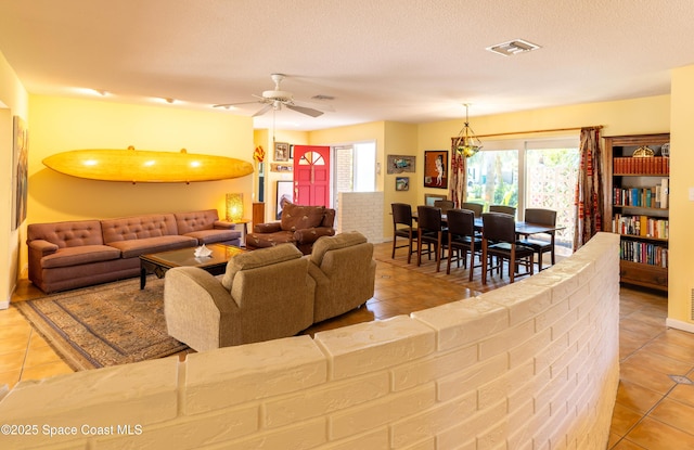 living room with a textured ceiling, light tile patterned floors, visible vents, and a ceiling fan