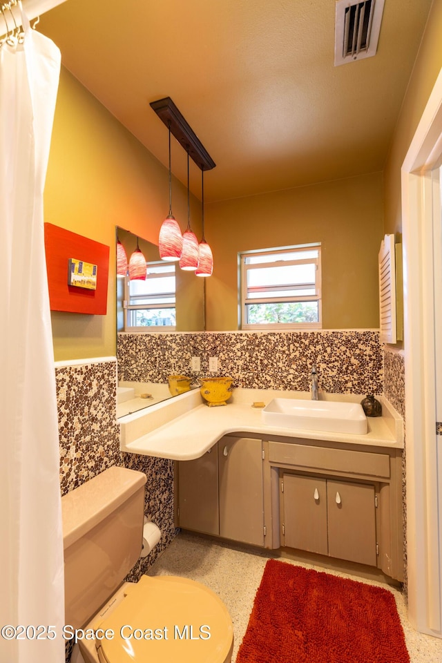 bathroom with a wainscoted wall, visible vents, toilet, vanity, and speckled floor