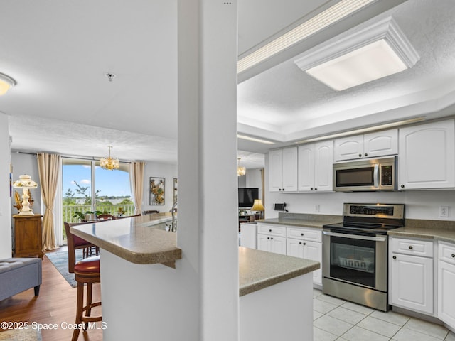 kitchen with white cabinetry, kitchen peninsula, appliances with stainless steel finishes, and an inviting chandelier