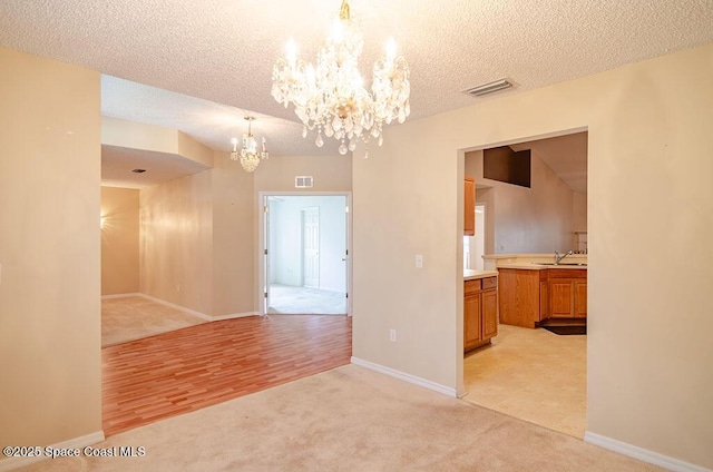 unfurnished room with sink, a textured ceiling, a notable chandelier, and light colored carpet