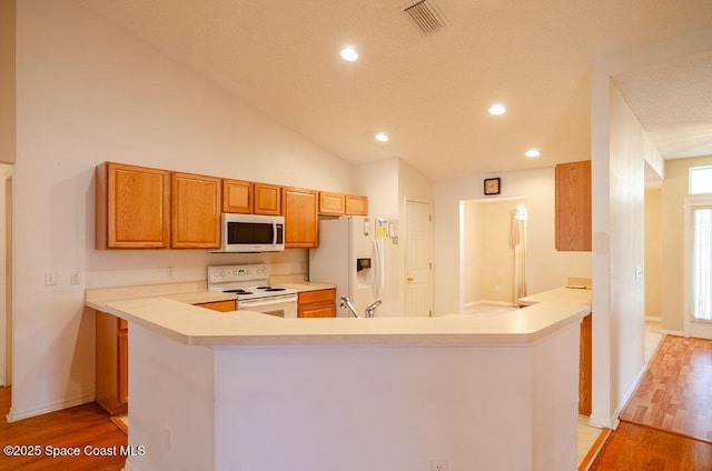 kitchen with high vaulted ceiling, white appliances, light wood-type flooring, and kitchen peninsula