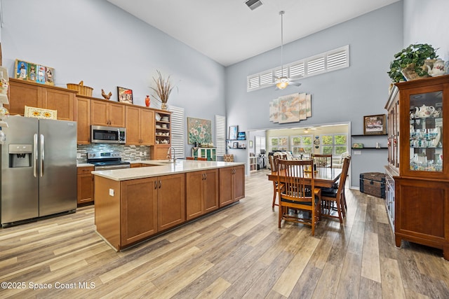 kitchen featuring a towering ceiling, decorative light fixtures, stainless steel appliances, tasteful backsplash, and sink