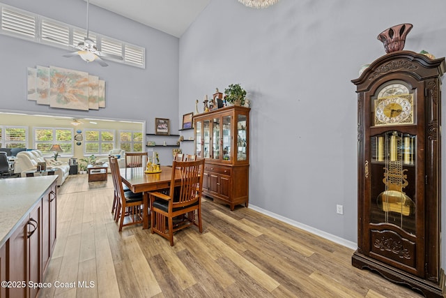 dining area with light hardwood / wood-style floors, a towering ceiling, and ceiling fan