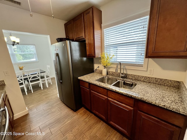 kitchen featuring sink, stainless steel fridge, light hardwood / wood-style floors, light stone counters, and a chandelier