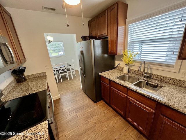 kitchen with sink, light stone counters, light hardwood / wood-style flooring, a chandelier, and appliances with stainless steel finishes