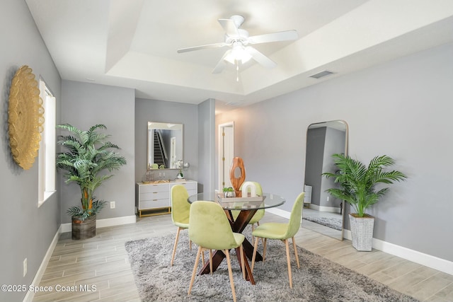 dining area with a raised ceiling, ceiling fan, and light hardwood / wood-style flooring