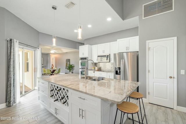 kitchen featuring light stone counters, a center island with sink, white cabinets, appliances with stainless steel finishes, and sink