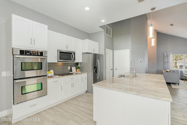 kitchen with light stone counters, decorative light fixtures, stainless steel appliances, an island with sink, and white cabinets