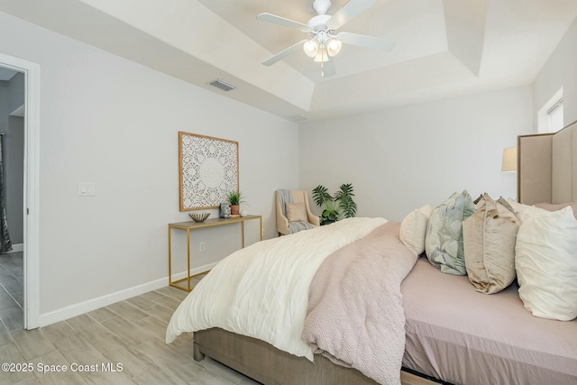 bedroom with ceiling fan, light hardwood / wood-style flooring, and a tray ceiling