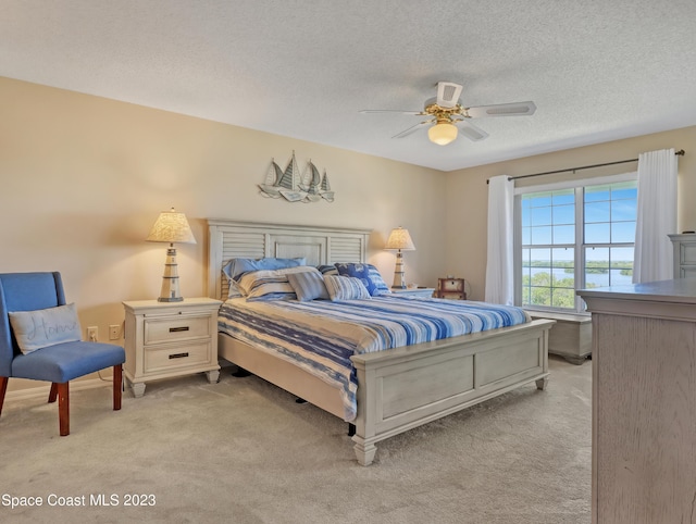 bedroom with ceiling fan, light carpet, and a textured ceiling