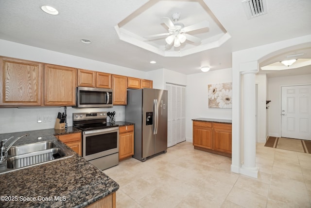 kitchen with appliances with stainless steel finishes, ornate columns, sink, a raised ceiling, and ceiling fan