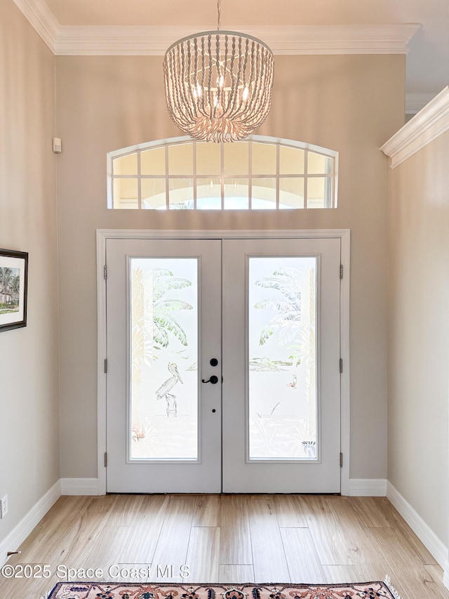 foyer with crown molding, light wood-type flooring, french doors, and a notable chandelier