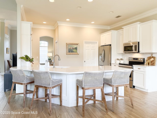 kitchen with stainless steel appliances, white cabinetry, sink, and a breakfast bar