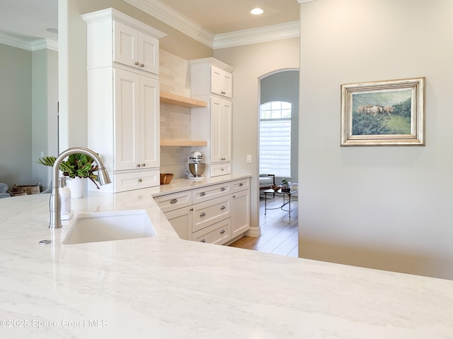 kitchen with white cabinetry, sink, ornamental molding, light stone countertops, and light wood-type flooring