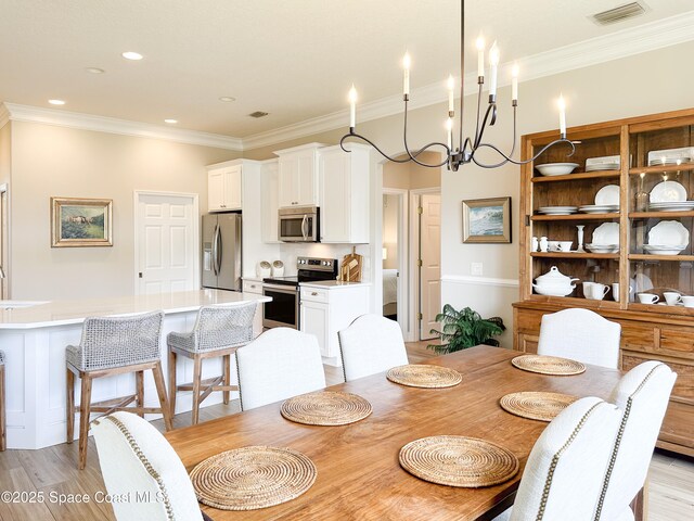 dining space with ornamental molding, a chandelier, and light wood-type flooring