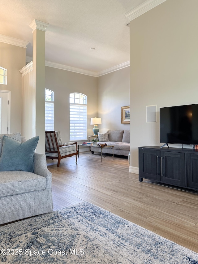 living room with decorative columns, ornamental molding, and light hardwood / wood-style flooring