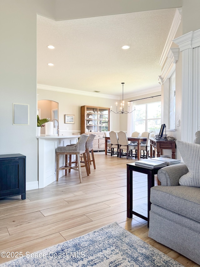 living room featuring crown molding, an inviting chandelier, and light wood-type flooring