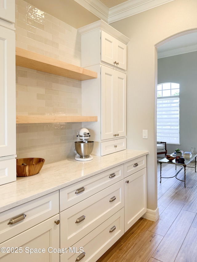 kitchen with light stone counters, white cabinetry, crown molding, and light wood-type flooring