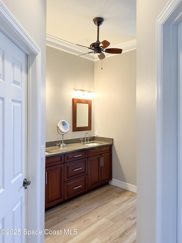 bathroom featuring vanity, wood-type flooring, ornamental molding, and ceiling fan