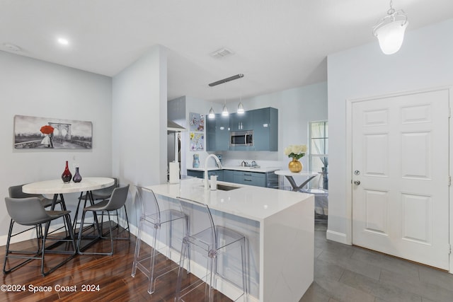 kitchen featuring blue cabinetry, stainless steel appliances, kitchen peninsula, pendant lighting, and a kitchen bar