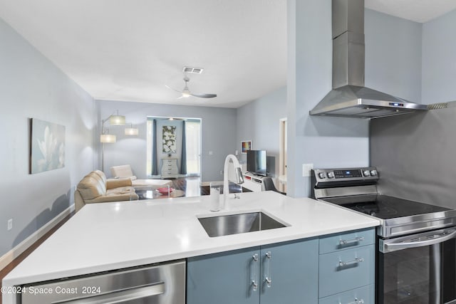 kitchen with wall chimney range hood, sink, ceiling fan, blue cabinetry, and appliances with stainless steel finishes