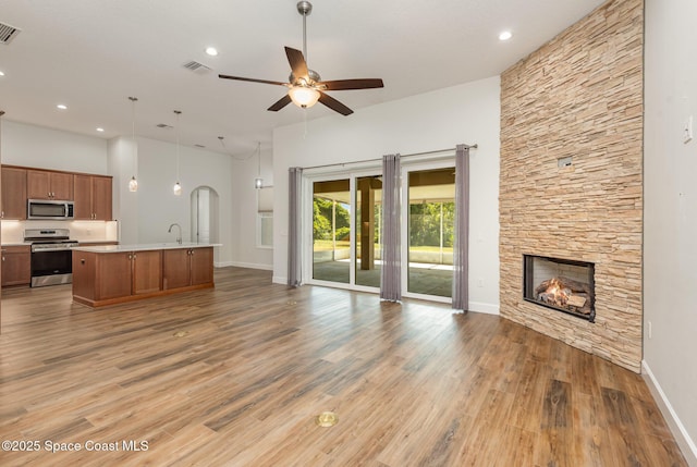 unfurnished living room with ceiling fan, sink, wood-type flooring, a fireplace, and a high ceiling