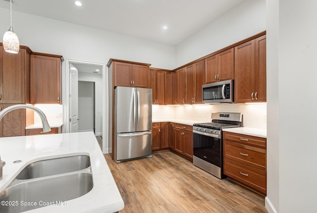 kitchen featuring sink, light wood-type flooring, decorative light fixtures, and appliances with stainless steel finishes