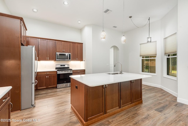 kitchen featuring appliances with stainless steel finishes, light wood-type flooring, a kitchen island with sink, sink, and pendant lighting