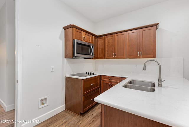 kitchen with black electric stovetop, light hardwood / wood-style floors, kitchen peninsula, and sink