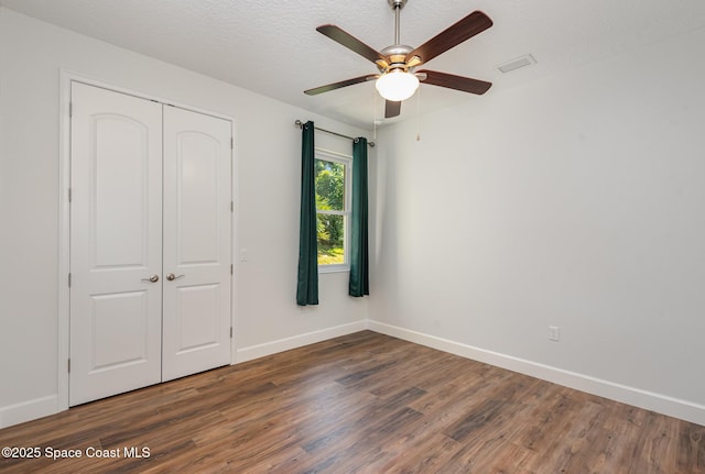 unfurnished bedroom with ceiling fan, a closet, dark wood-type flooring, and a textured ceiling