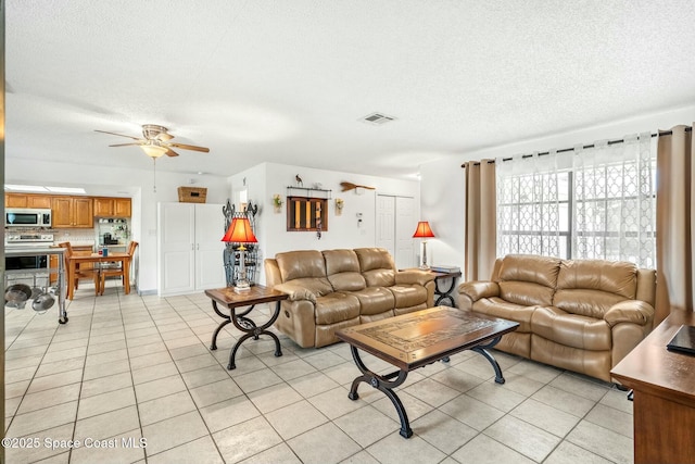 living room with ceiling fan, light tile patterned flooring, and a textured ceiling