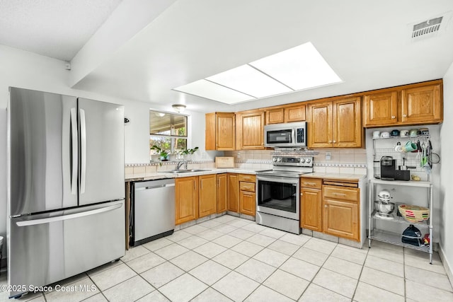 kitchen featuring a skylight, backsplash, appliances with stainless steel finishes, light tile patterned flooring, and sink