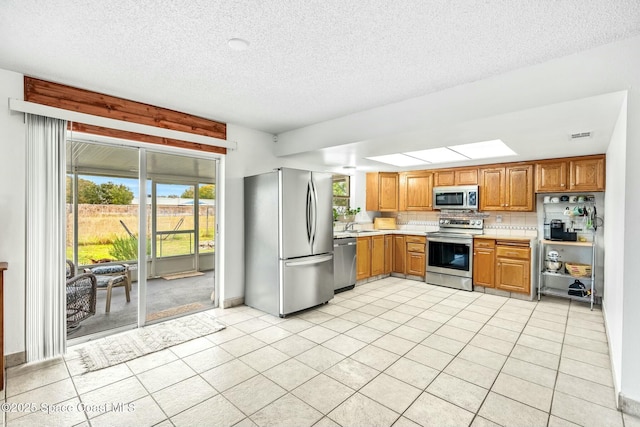 kitchen with stainless steel appliances, a textured ceiling, decorative backsplash, sink, and light tile patterned flooring