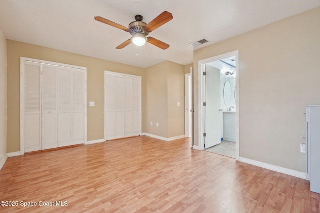 unfurnished bedroom with ensuite bath, light wood-type flooring, two closets, and ceiling fan