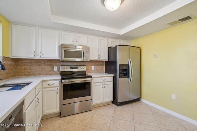 kitchen with appliances with stainless steel finishes, decorative backsplash, a tray ceiling, sink, and white cabinetry