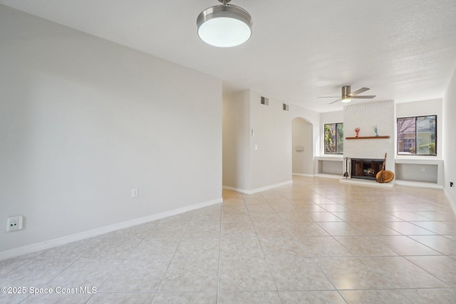 unfurnished living room with ceiling fan, a brick fireplace, a textured ceiling, and light tile patterned floors