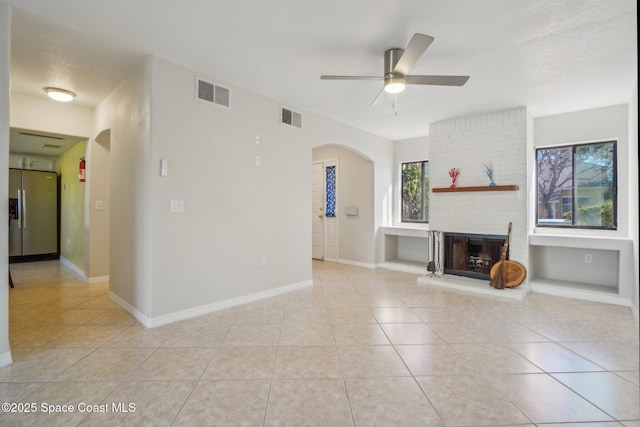 unfurnished living room with ceiling fan, light tile patterned flooring, a fireplace, and a textured ceiling